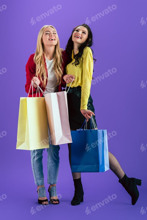 Preview: Cheerful girls posing with colorful shopping bags on purple background