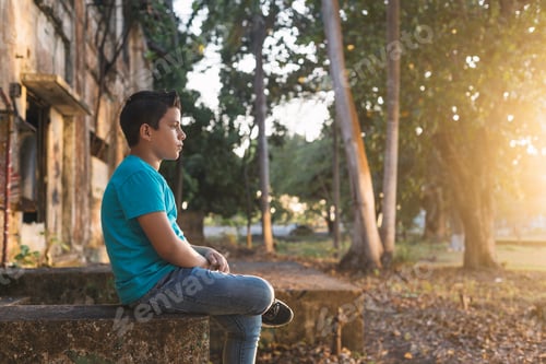 Preview: Hispanic boy sitting on some ruins looking at the horizon in the forest, with a serious expression.