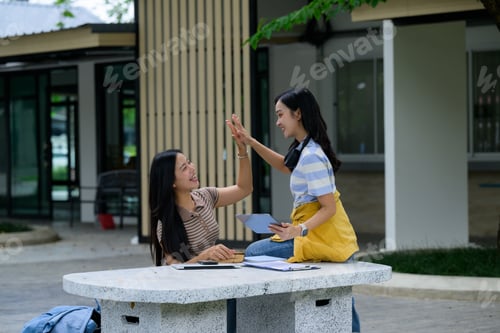 Preview: Two happy students giving high five after finishing studying together outdoors