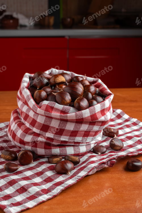 Preview: Fresh chestnuts in a red checkered cloth bag on a wooden kitchen table
