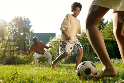 Preview: Legs of barefoot girl kicking ball to her brother while playing on green lawn
