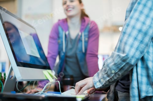 Preview: Two people at a computer repair shop, one typing and checking a monitor display.