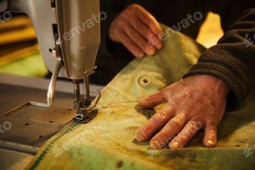 Preview: Close up of a man in a sailmaker's workshop sewing a sail with a sewing machine.