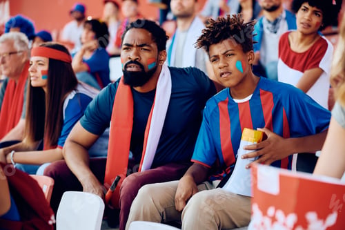 Preview: Black sports fan and his son watching the game from the stadium stands.