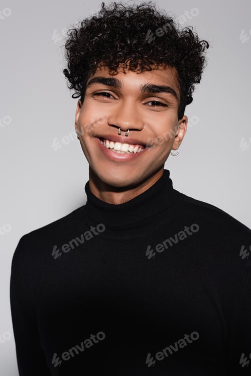 Preview: curly african american man in black turtleneck sweater smiling isolated on grey