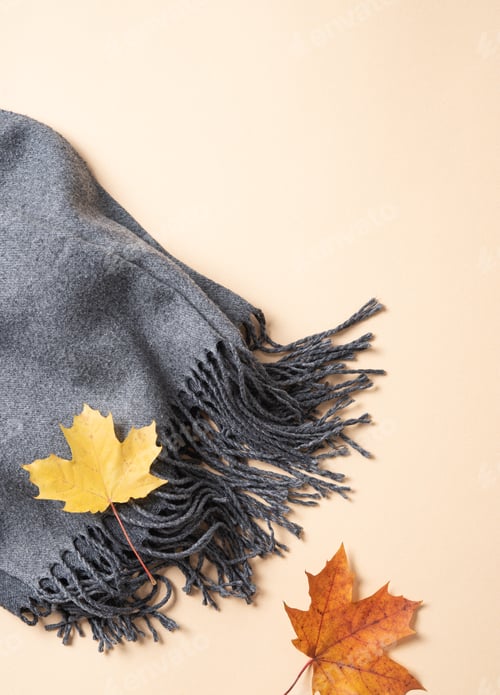 Preview: Concept flat lay with autumn maple leaves and a cozy gray scarf on a light orange background