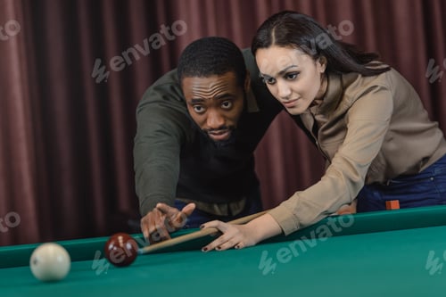 Preview: young attractive multiethnic man and woman playing in pool at bar