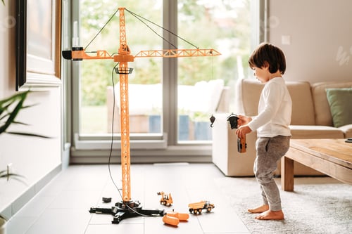 Vista previa: Little toddler boy playing with big construction building crane toy at home in living room.