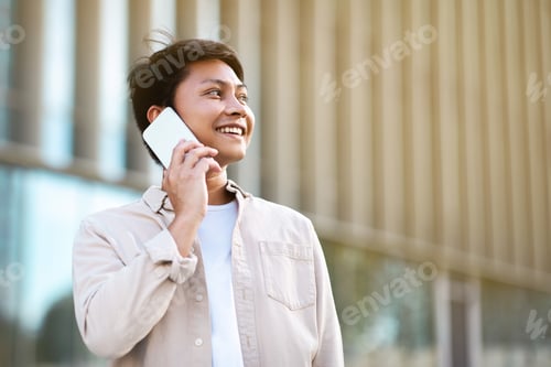 Preview: Young asian guy talking on phone while walking by park