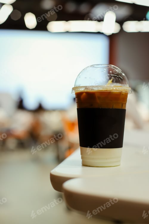 Preview: Close up glass of ice latte with blurred people in business workshop and presentation.