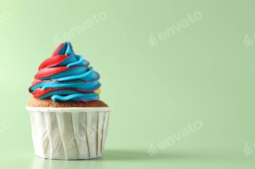 Preview: Tasty cupcake with colorful cream on light green background, closeup. Space for text