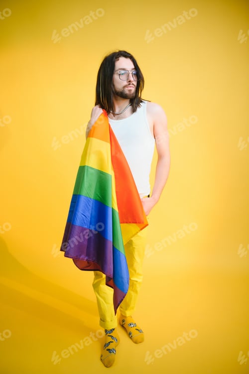 Preview: gay man with a gay pride flag smiling and looking away on yellow background