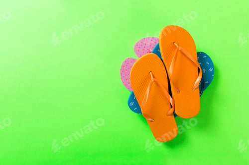 Preview: A lot of colored flip flops on green background. Top view with copy space