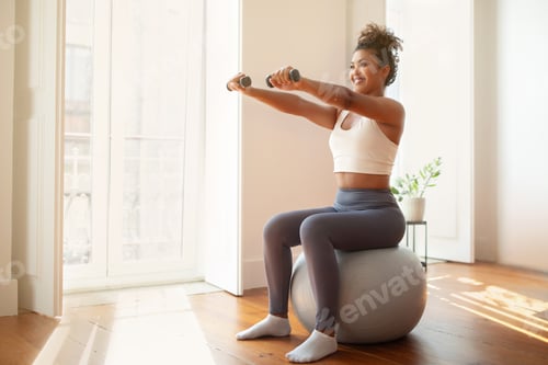 Woman Exercising with Dumbbells Indoors on Exercise Ball