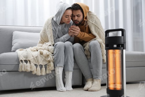 Preview: Young couple getting warm near electric heater at home