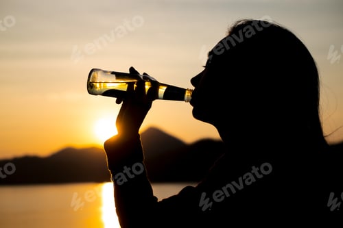 Preview: Silhouette woman drinking water on the beach at dusk