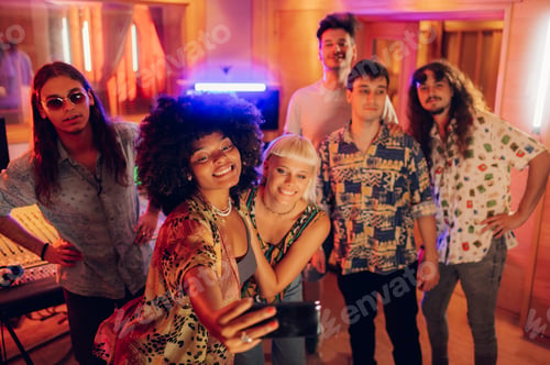 Preview: Band member taking a photo of her band mates and herself in a music studio.