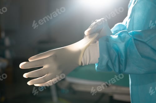 Preview: Midsection of biracial female surgeon wearing surgical gown and gloves in operating theatre