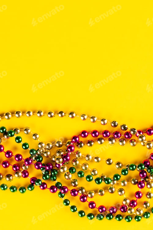 Preview: Composition of colourful mardi gras beads on yellow background with copy space
