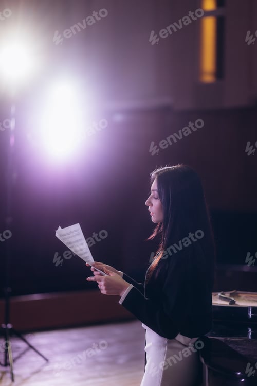 Preview: Portrait of a female musician with sheet music on the stage, light from spotlights