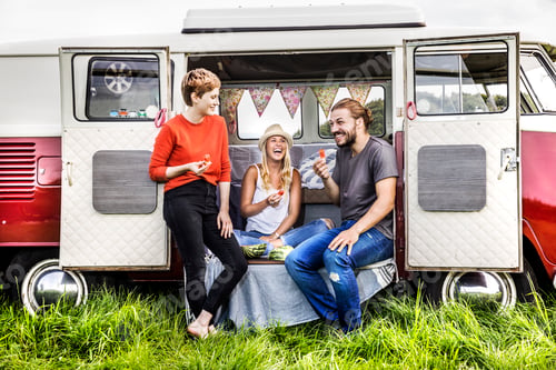 Preview: Happy friends having picnic in a van parked on field