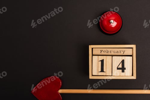 Preview: top view of heart-shaped arrow near wooden cubes with 14 february lettering and bell on black