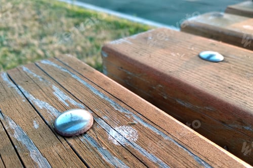 Preview: Close-up of wooden boards fastened with metal nails on a bench outdoors.
