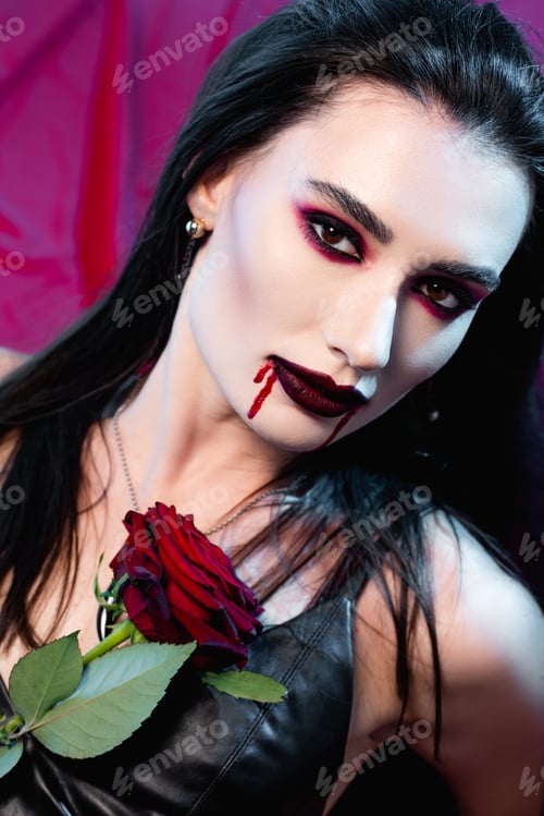 Preview: pale woman with blood on face and rose looking at camera on red