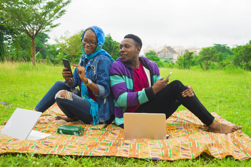 Preview: Happy Nigerian couple using the cellphones while on a picnic on a grass-covered meadow