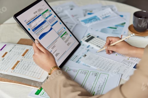 Preview: Close up table with utility bills and paper documents. Unknown woman holds tablet writes down notes