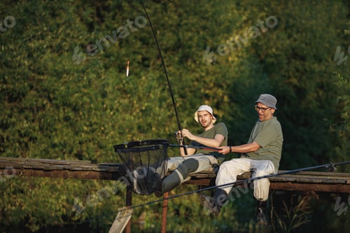 Preview: Two fishermen with fishing rods on a footbridge near the lake at summer