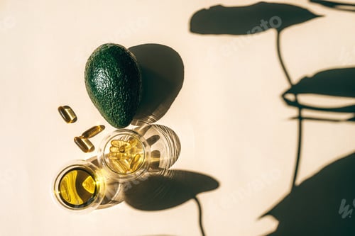 Preview: Capsules fish oil omega-3 in glass cups and an avocado with a shadow of monstera leaves
