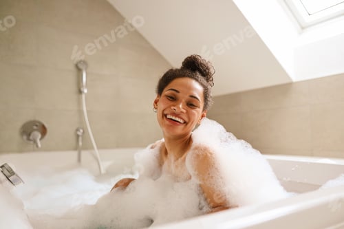 Preview: A happy woman is bathing in a foamfilled bathtub, smiling at the fixture