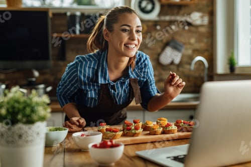 Preview: Happy woman preparing food and vlogging over laptop in the kitchen.