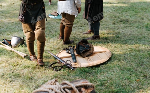 Preview: Wooden shield, swords, spears and viking feet on grass outdoors. Medieval weapons