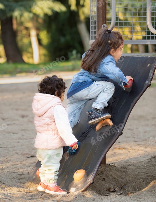 Preview: Two little latin girls playing and climbing on a slide at the playground