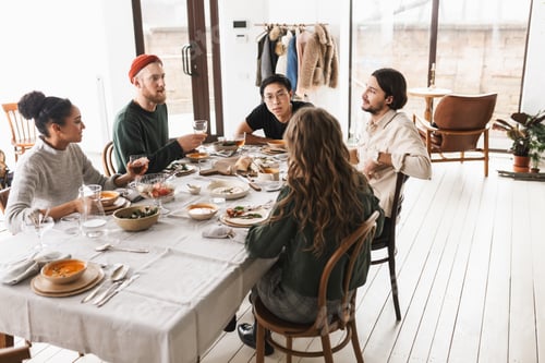 Preview: Young international friends sitting at the table full of food dreamily talking to each other