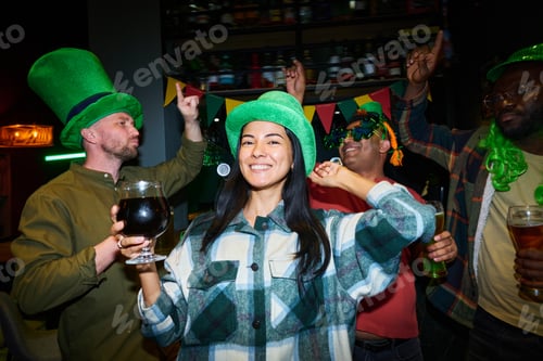 Preview: Young cheerful woman in grey flannel and green hat dancing among friends