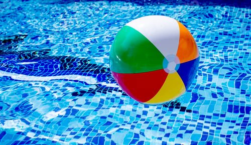 Preview: Colorful beach ball floats on the surface of a pool reflecting sunlight on a summer day