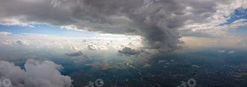 Preview: Aerial view from airplane window at high altitude of distant city covered with puffy cumulus clouds