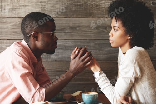 Preview: African American young couple sitting at a cafe table: black man in glasses holding her beautiful wi