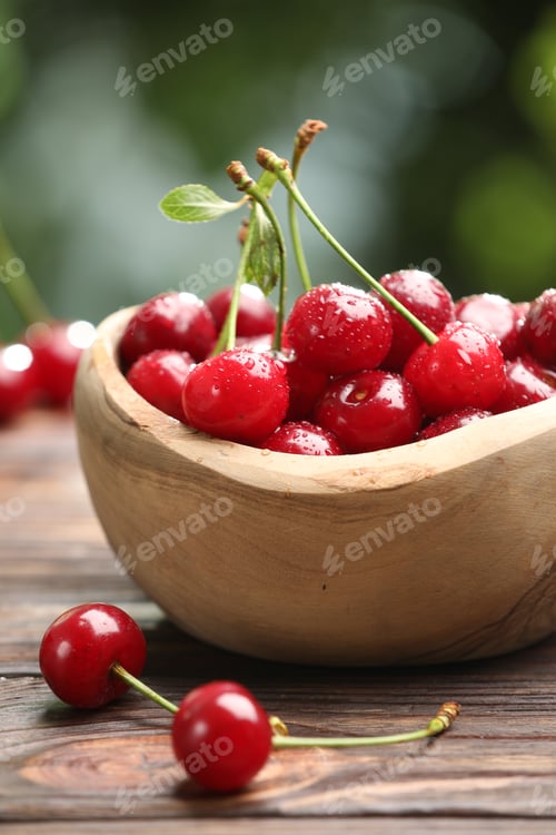 Preview: Fresh wet cherries in bowl on wooden table against blurred green background, closeup