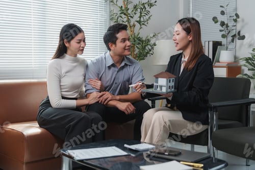 Preview: Real estate agent showing house model to young couple in office