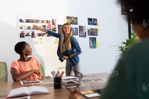 Preview: Diverse group of happy business colleagues brainstorming pointing at photos in meeting room