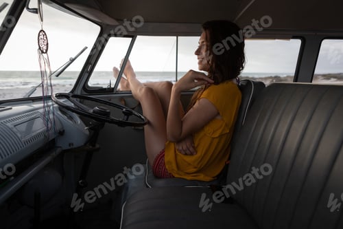 Preview: Beautiful woman relaxing in camper van with his foot outside at beach