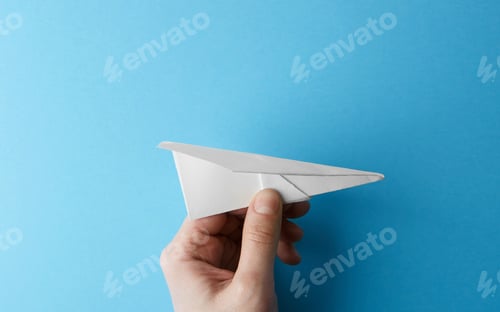 Preview: Paper plane on blue background holding in male hand. Travel and tourism concept. Horizontal.