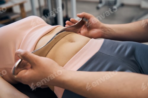 Preview: Chiropractor massages woman using IASTM tool for scraping muscles in rehab clinic gym closeup