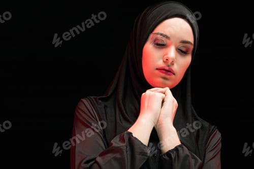 Preview: Portrait of beautiful serious young muslim woman wearing black hijab with closed eyes as praying