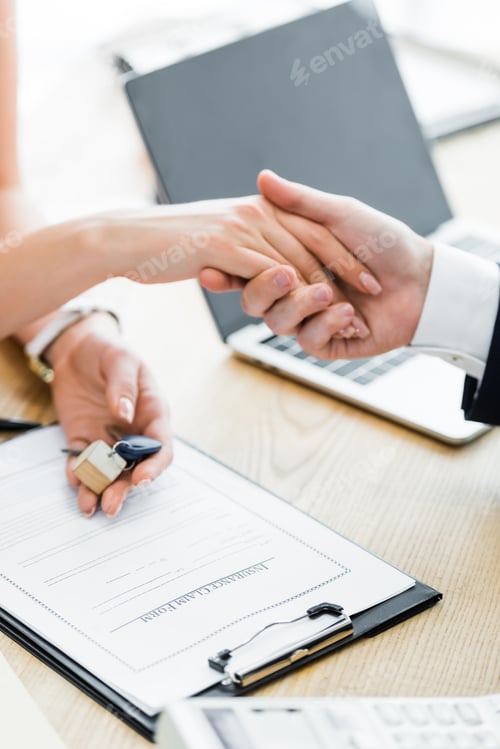 Preview: cropped view of woman holding keys in hand and shaking hands with realtor