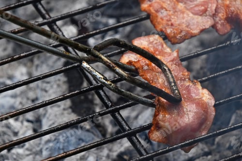 Preview: Tongs with bacon slice cooked on bbq grill